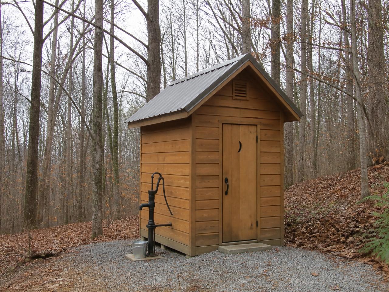 Simple wooden vault toilet and water pump at the edge of the woods